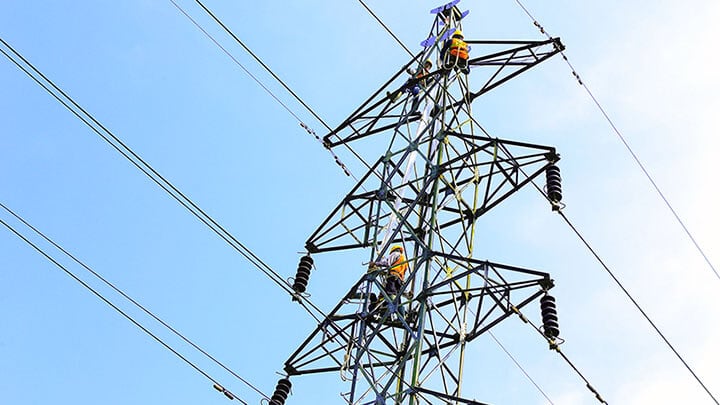 Three workers in safety gear working on a transmission tower