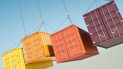 Four shipping containers of varying colors being suspended in the air by chains